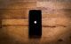 An iPhone laying face up on a wooden table, displaying the Apple logo startup screen.