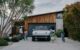 A Rivian electric vehicle site in a driveway, surrounded children following their parents into their home, showcasing the car's space and sleek design.