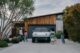 A Rivian electric vehicle site in a driveway, surrounded children following their parents into their home, showcasing the car's space and sleek design.