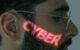 A close-up of a man's face illuminated by glowing green cyber text reflecting across his skin, symbolizing cybersecurity and digital interfaces.