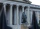 The statue of Albert Gallatin in front of the neoclassical Treasury Building in Washington, D.C., featuring grand columns and historic architecture.