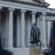 The statue of Albert Gallatin in front of the neoclassical Treasury Building in Washington, D.C., featuring grand columns and historic architecture.